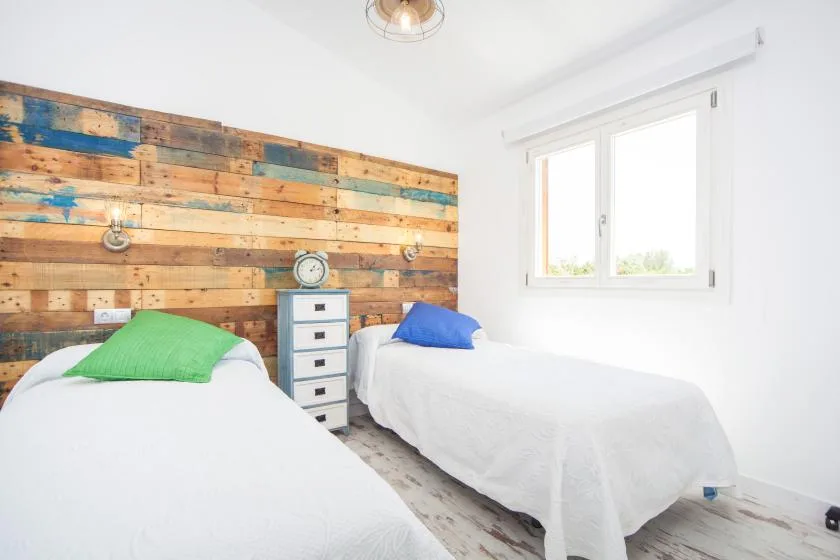 A bright bedroom with two single beds beside a large window.