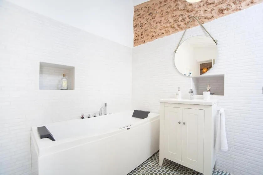 A bright bathroom with a bathtub, sink, and round mirror.