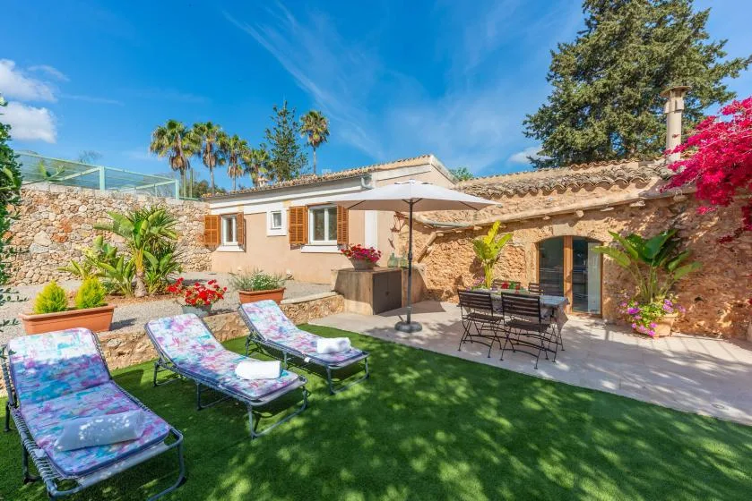 A sunny garden patio with loungers, outdoor seating, and a stone house.