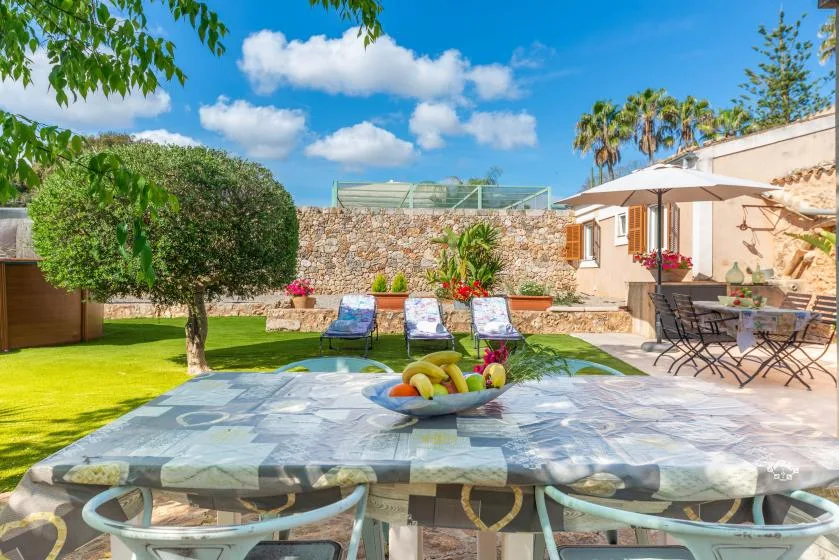 A sunny outdoor patio with a dining table, garden seating, and a stone wall.