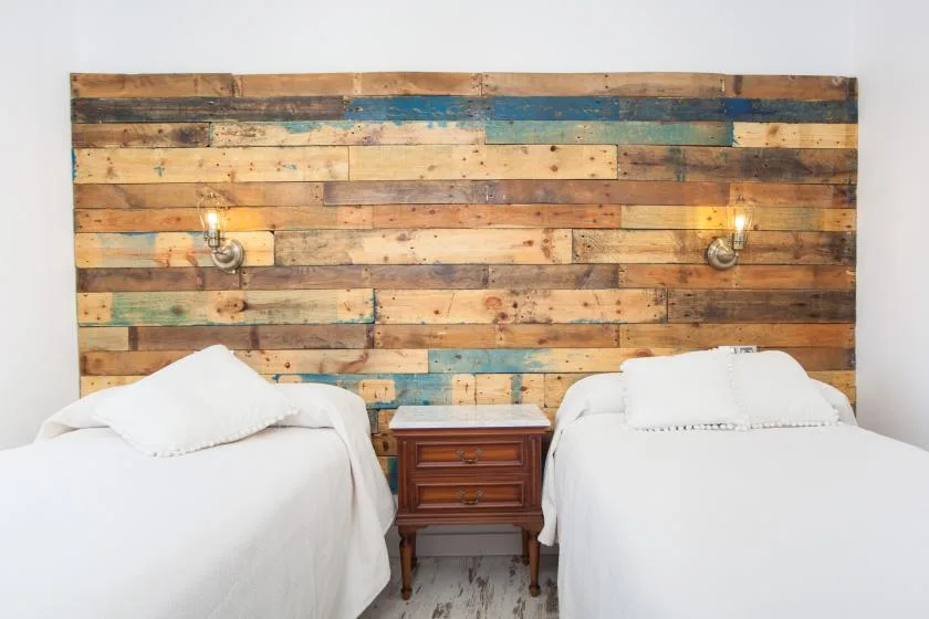 A bedroom with two beds and a colorful wooden plank wall behind them.
