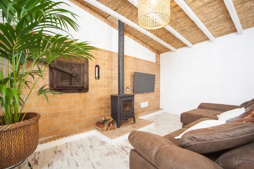 A rustic living room with brown seating, a stove, and exposed ceiling beams.