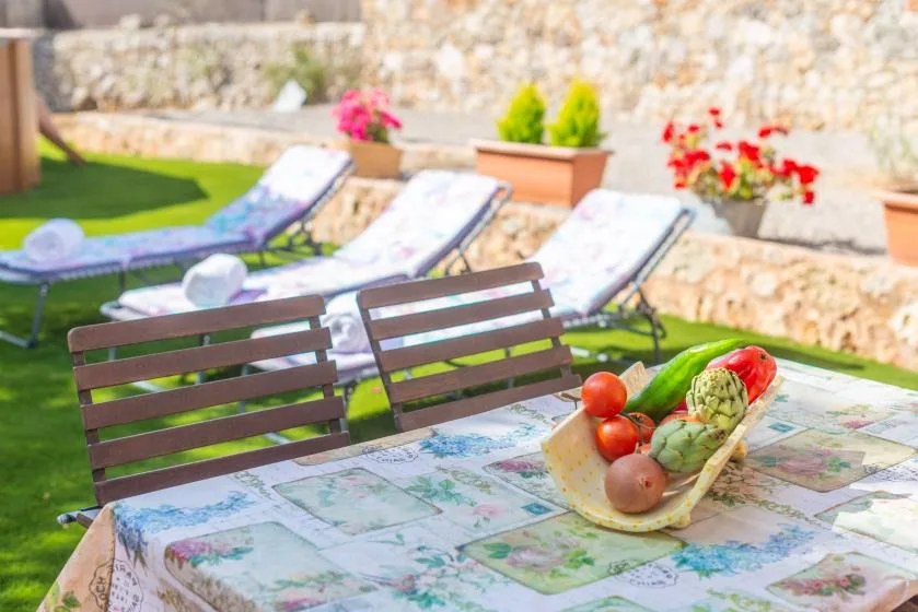 An outdoor dining table with fresh produce sits beside lawn seating and sun loungers.