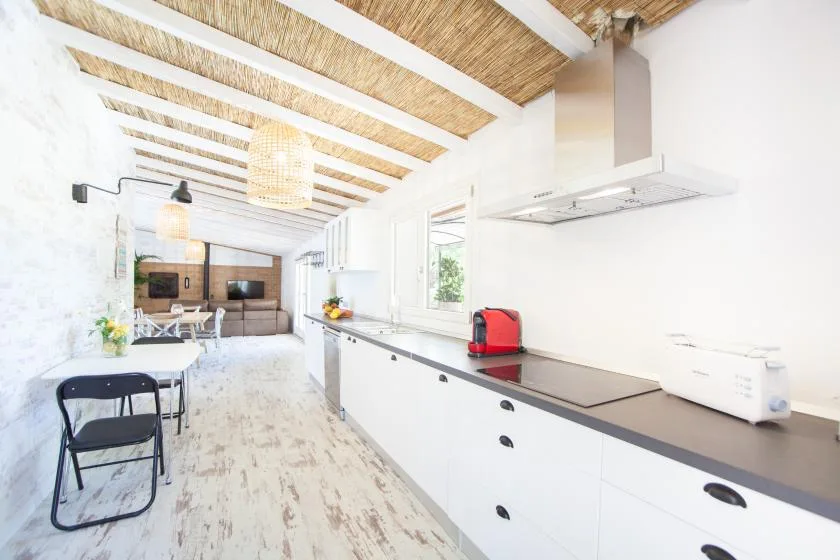 A bright open kitchen and dining area with a long counter and exposed ceiling beams.