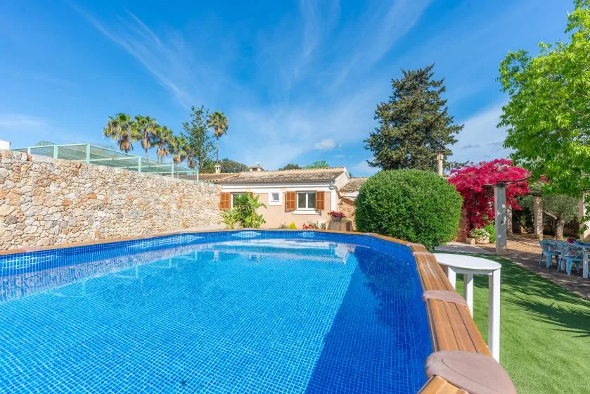 An outdoor swimming pool beside a low house and landscaped garden.