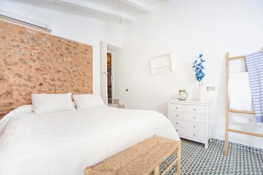 A bright bedroom with white bedding and a woven bench at the foot of the bed.