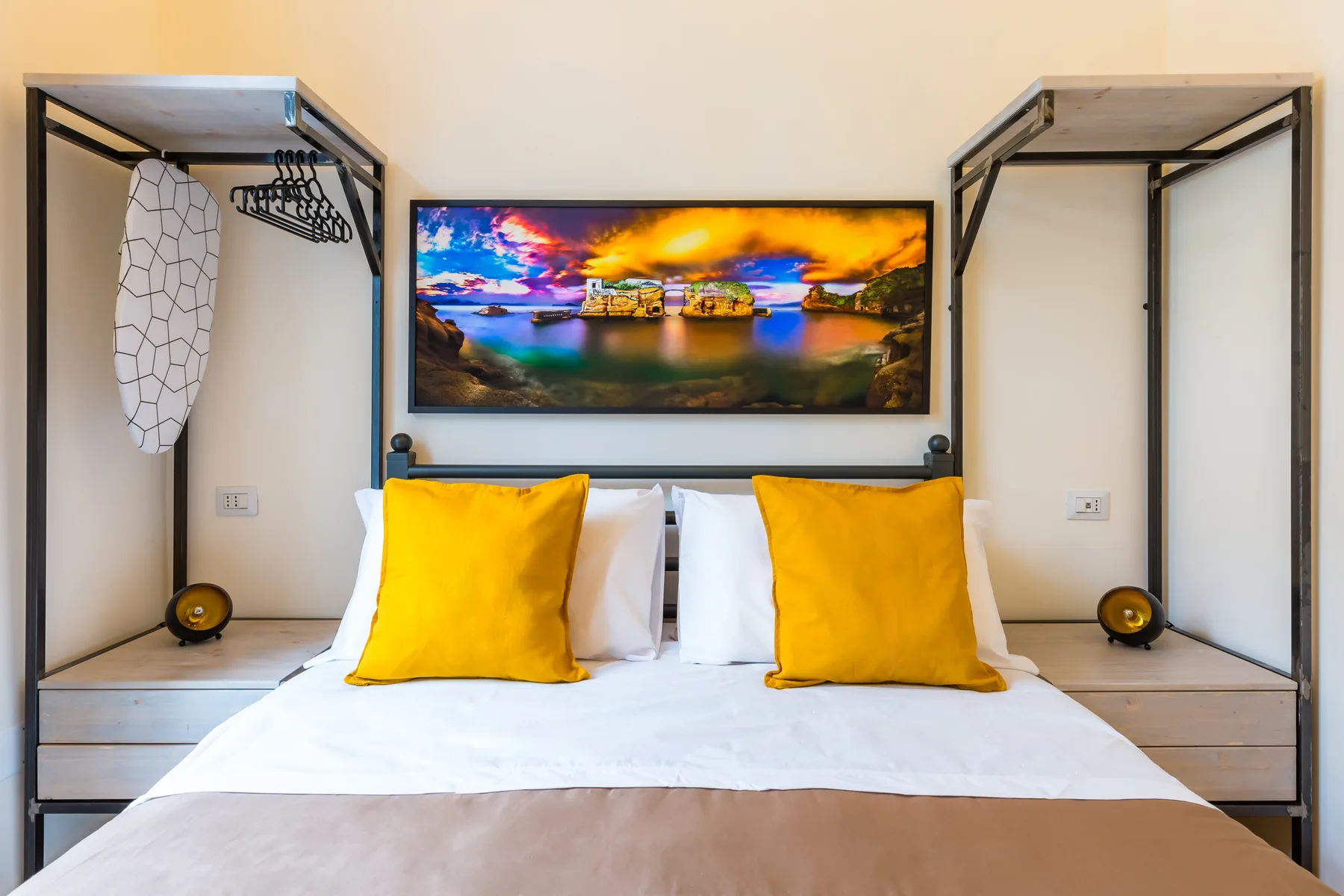 Un dormitorio con una cama, almohadas amarillas y un cuadro colorido de paisaje encima.