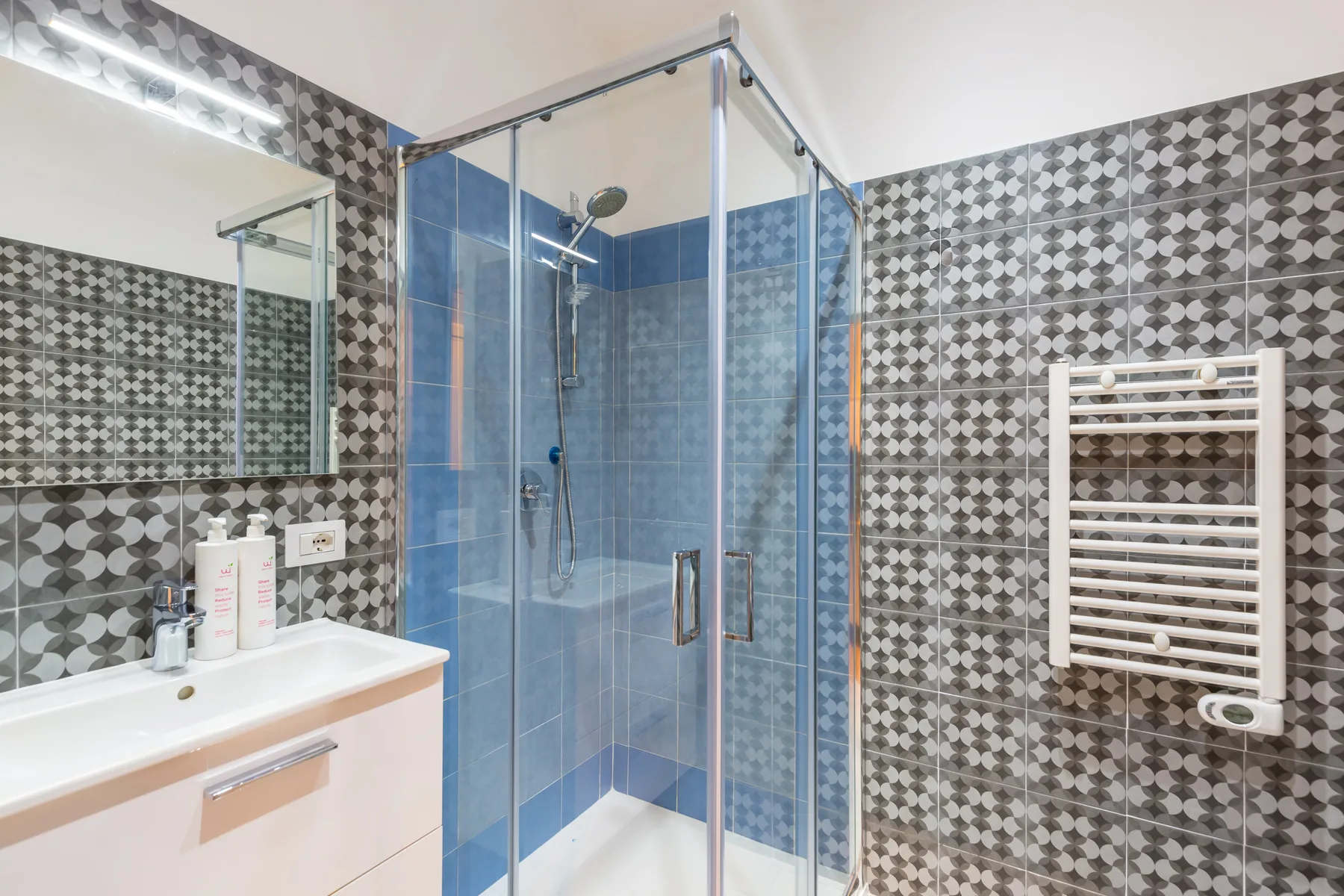 Un baño con azulejos, ducha de vidrio, lavabo y toallero mural.