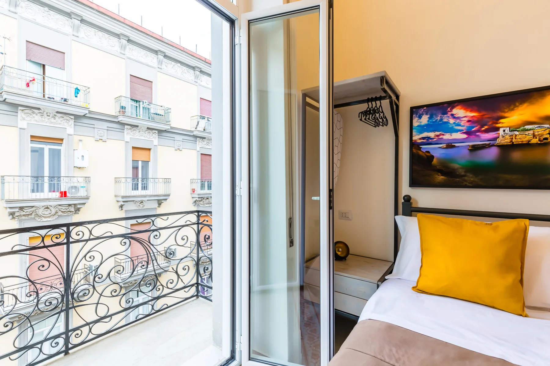 Un dormitorio con ropa de cama blanca y un cojín amarillo junto a una ventana grande.
