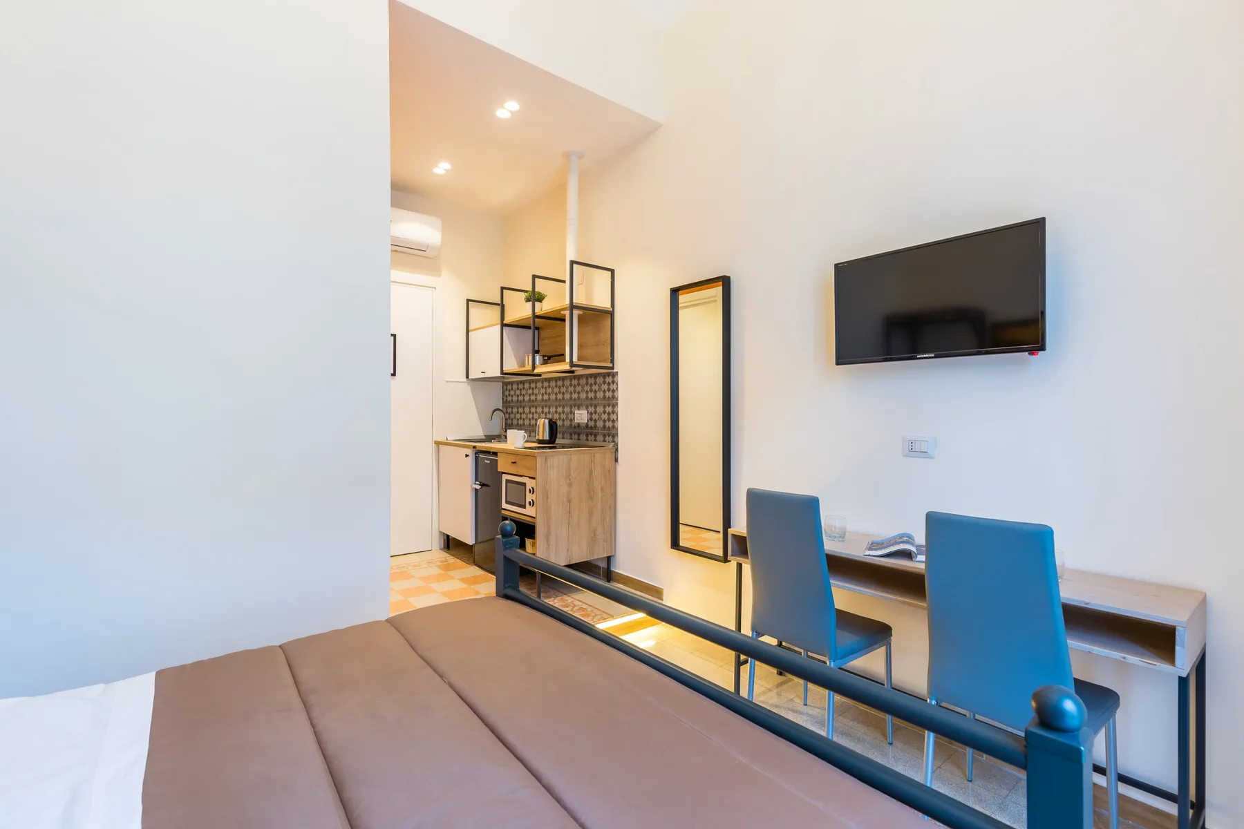 Un estudio compacto con una cama, sillas de comedor y un televisor montado en la pared.