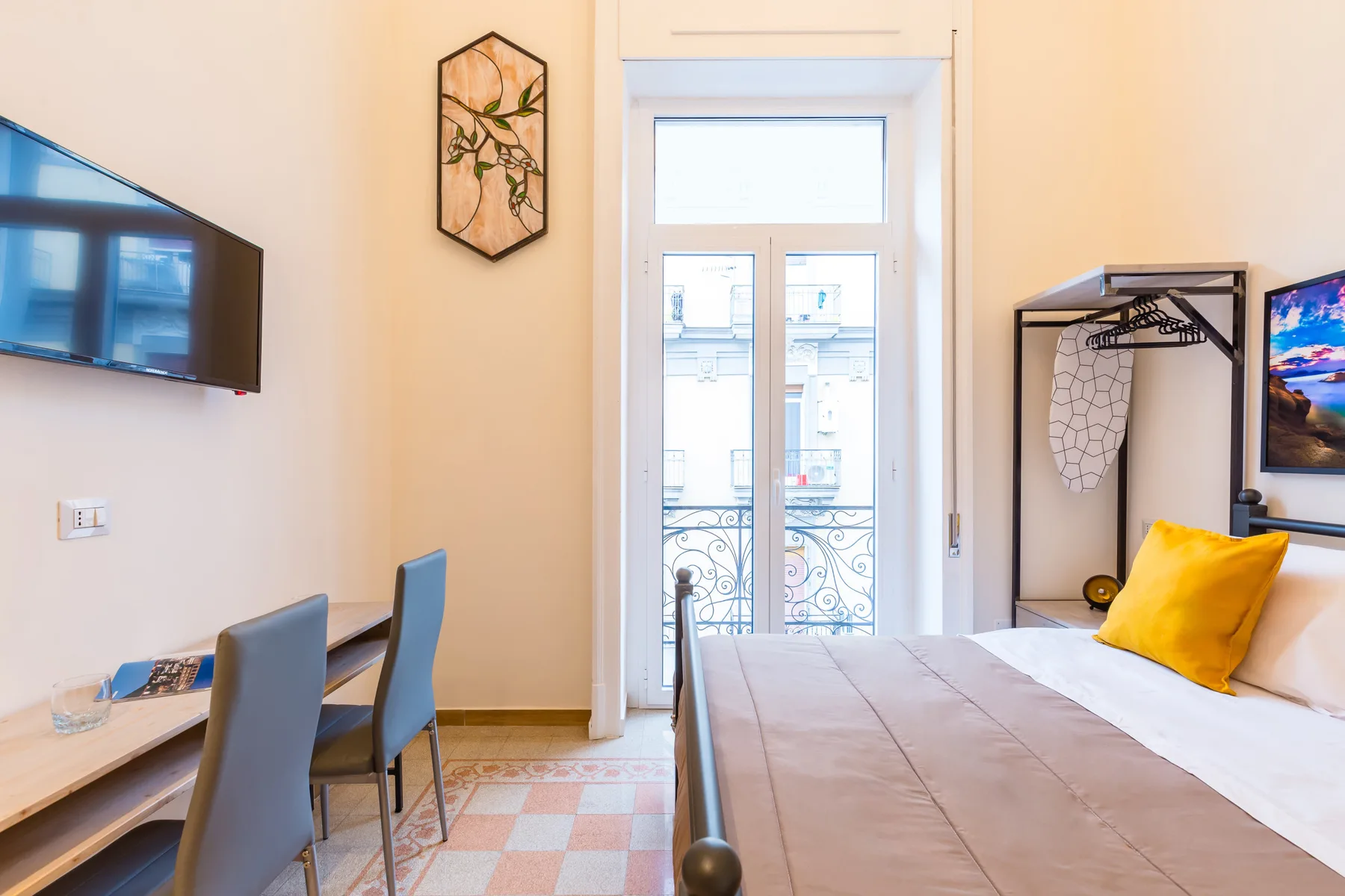 Un dormitorio con cama, escritorio y altas puertas de vidrio que dan a un balcón.