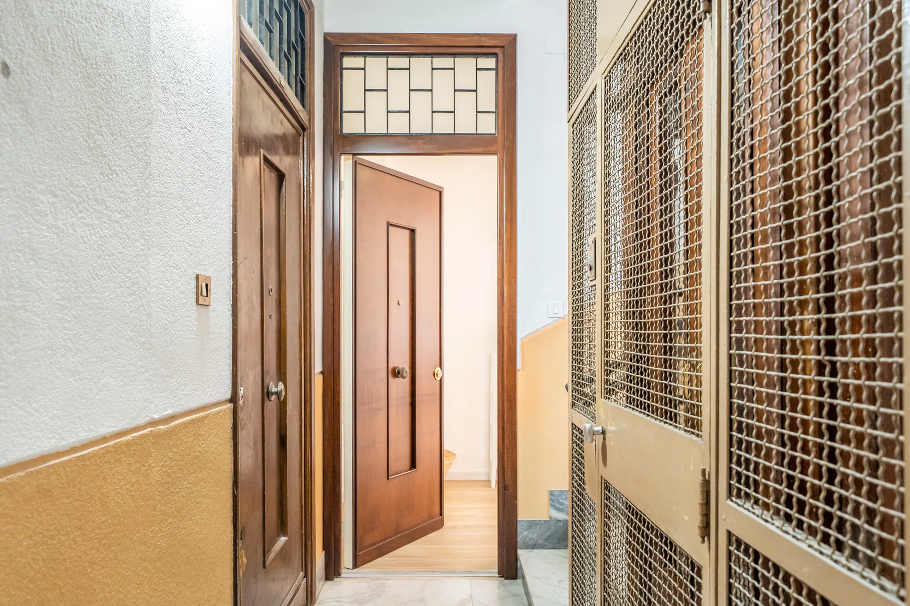 Un pasillo con puertas de madera y rejas metálicas de malla a un lado.