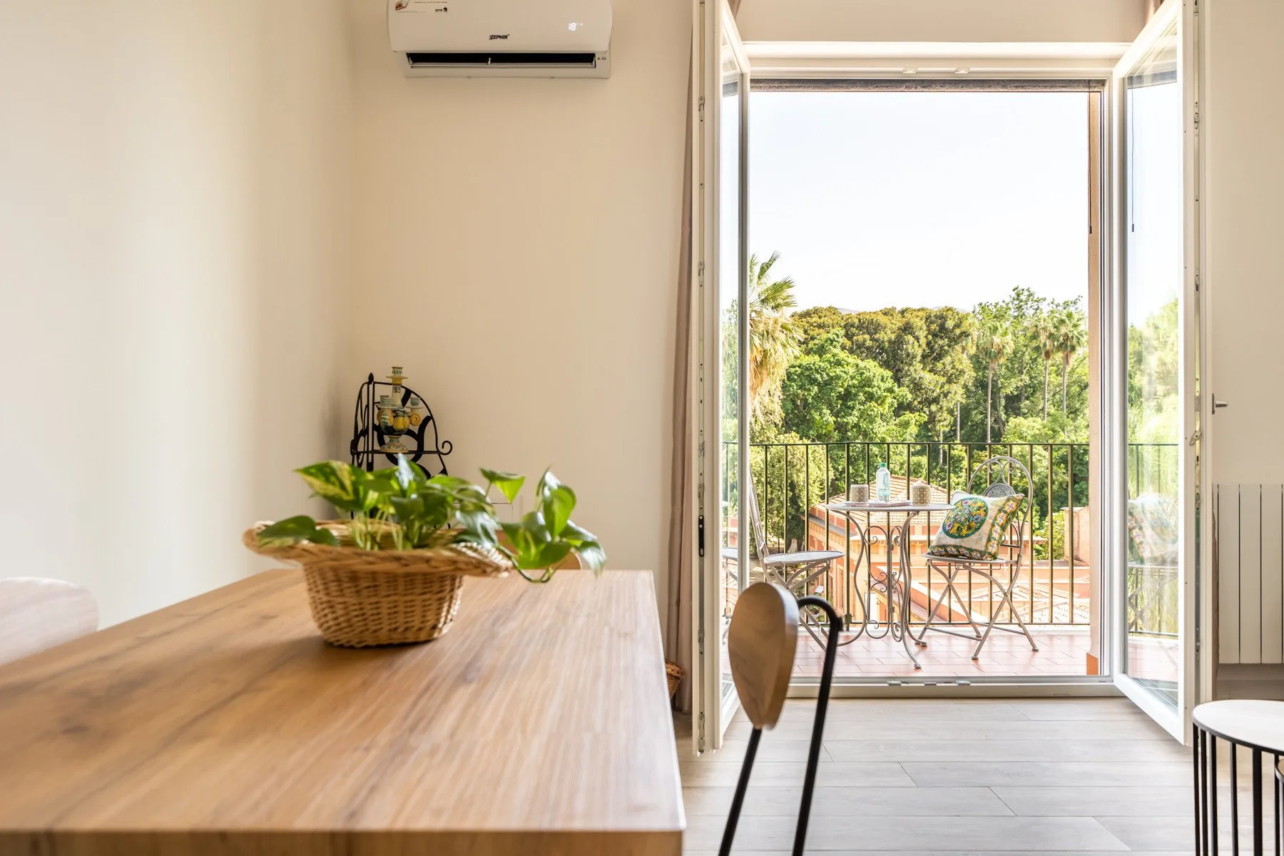 Un comedor se abre a un balcón soleado con asientos al aire libre y vegetación.