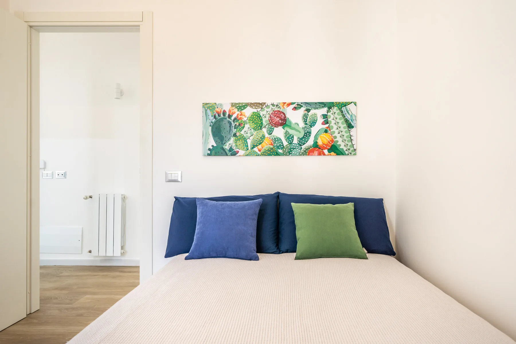 Un dormitorio con una cama, cojines coloridos y un pequeño cuadro floral.