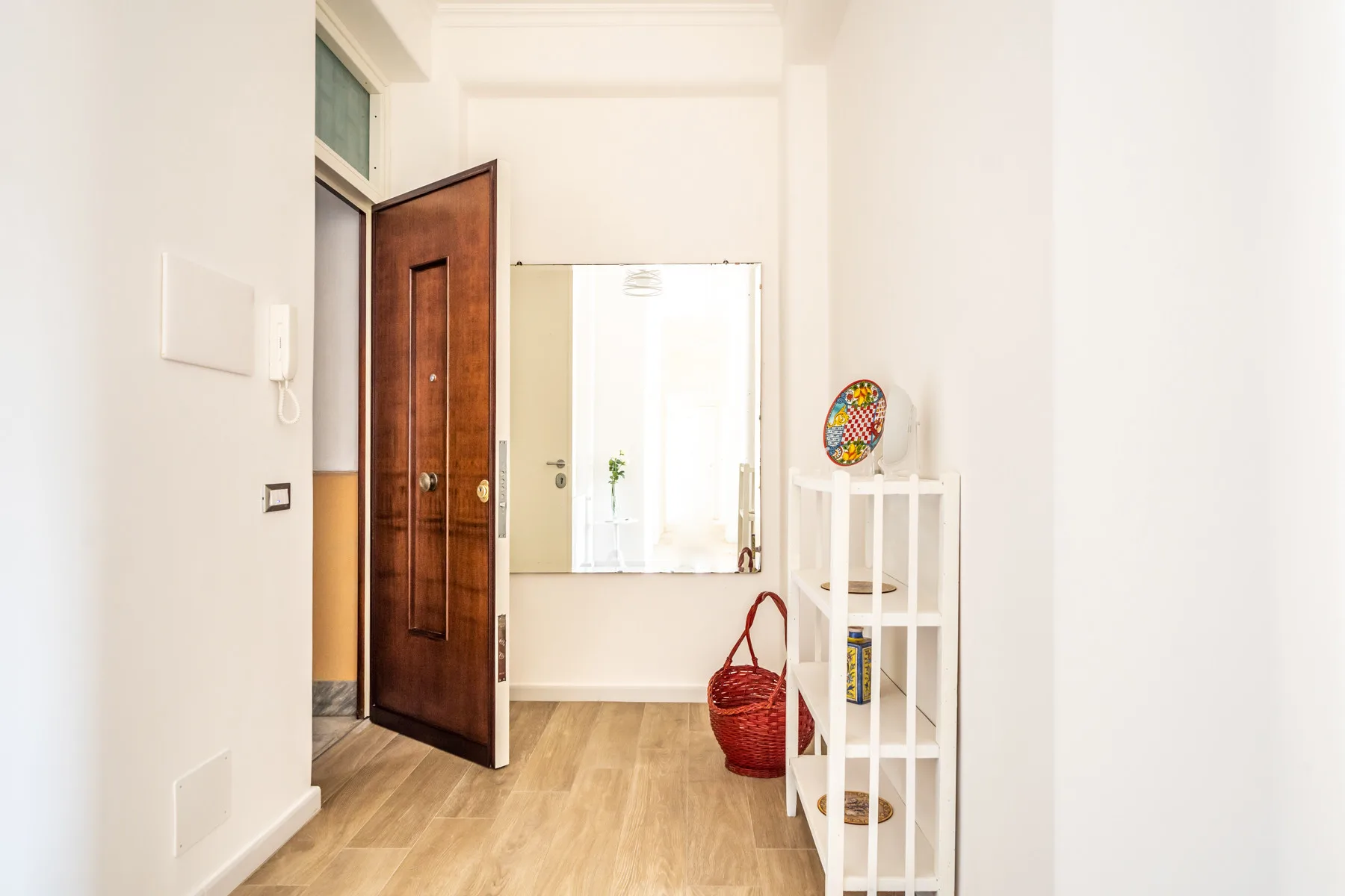 Un recibidor luminoso con una puerta de madera abierta y un espejo en la pared.