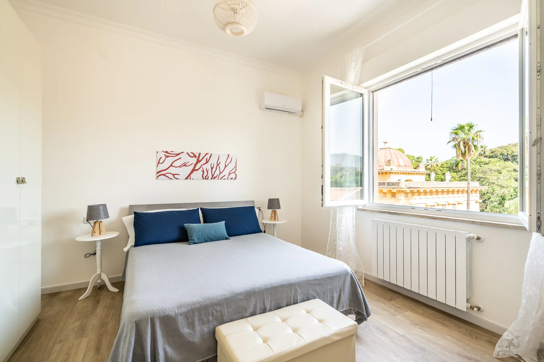 Un dormitorio luminoso con una cama junto a una ventana abierta con vistas a la vegetación.