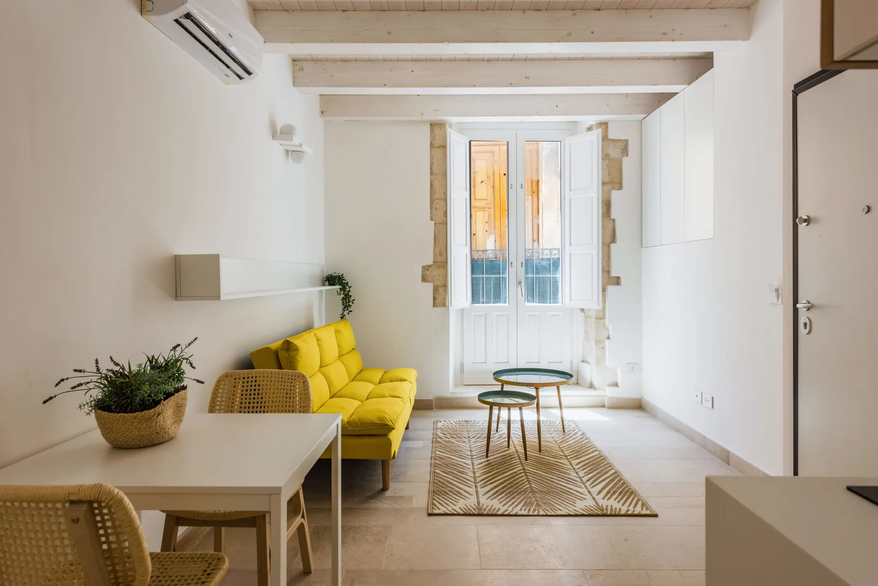 A bright living room with yellow seating, a dining table, and tall windows.