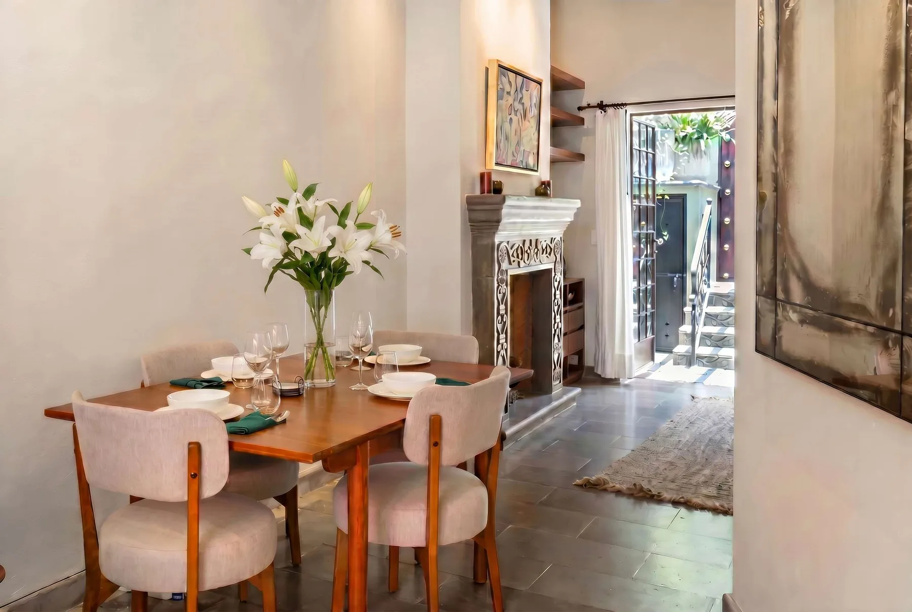 A dining area with a set table, white flowers, and a fireplace.