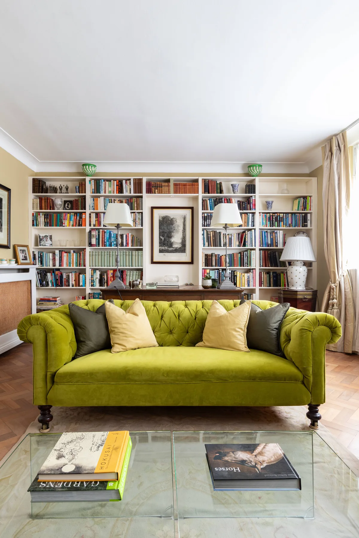 A living room features a green sofa in front of bookshelves filled with books.
