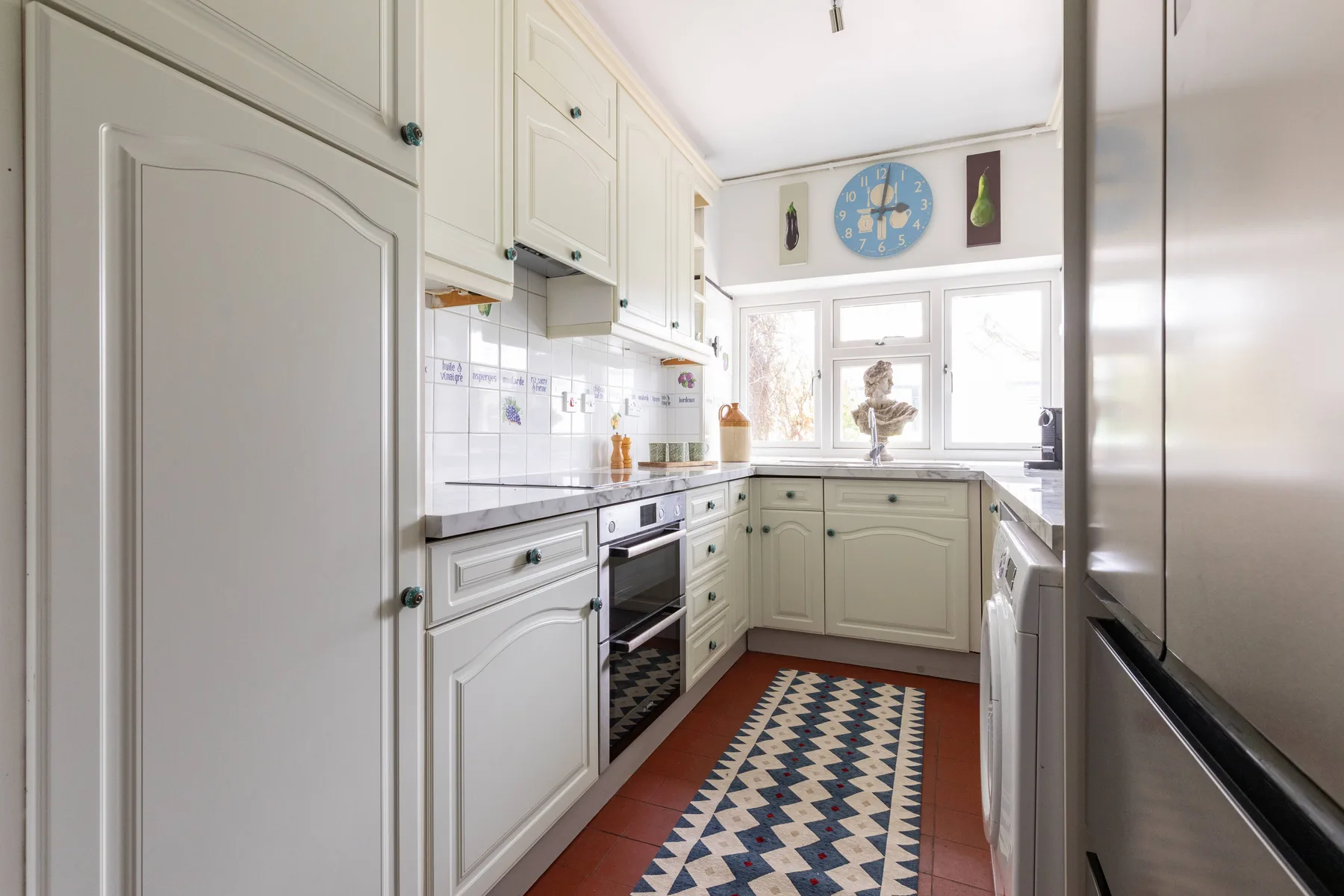 A bright kitchen with white cabinetry, tiled counters, and a patterned runner.