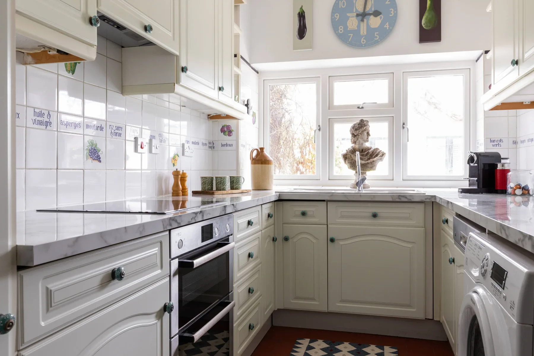 A bright kitchen with pale cabinets and counters beneath a wide window.