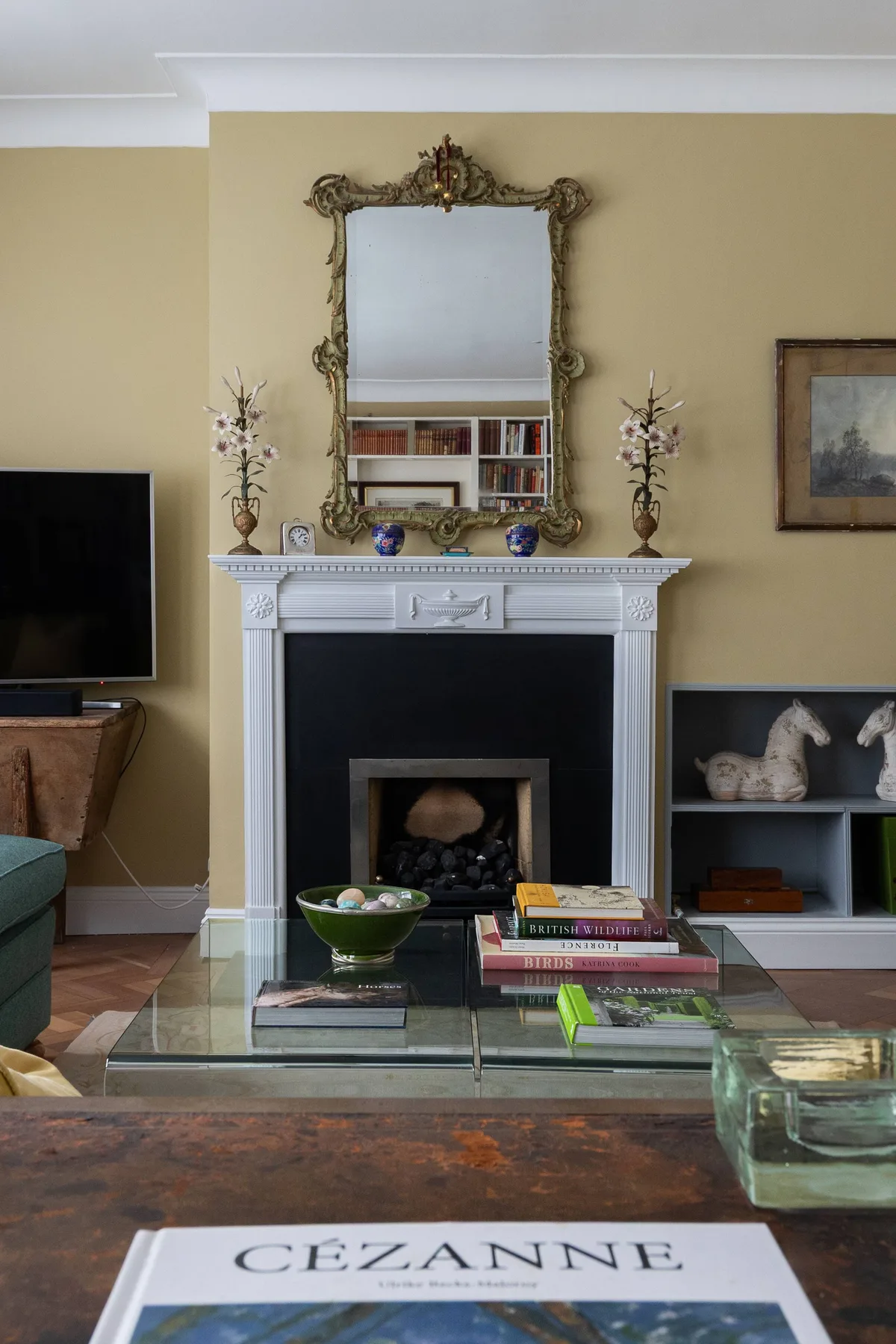 A living room with a white fireplace, ornate mirror, and glass coffee table.