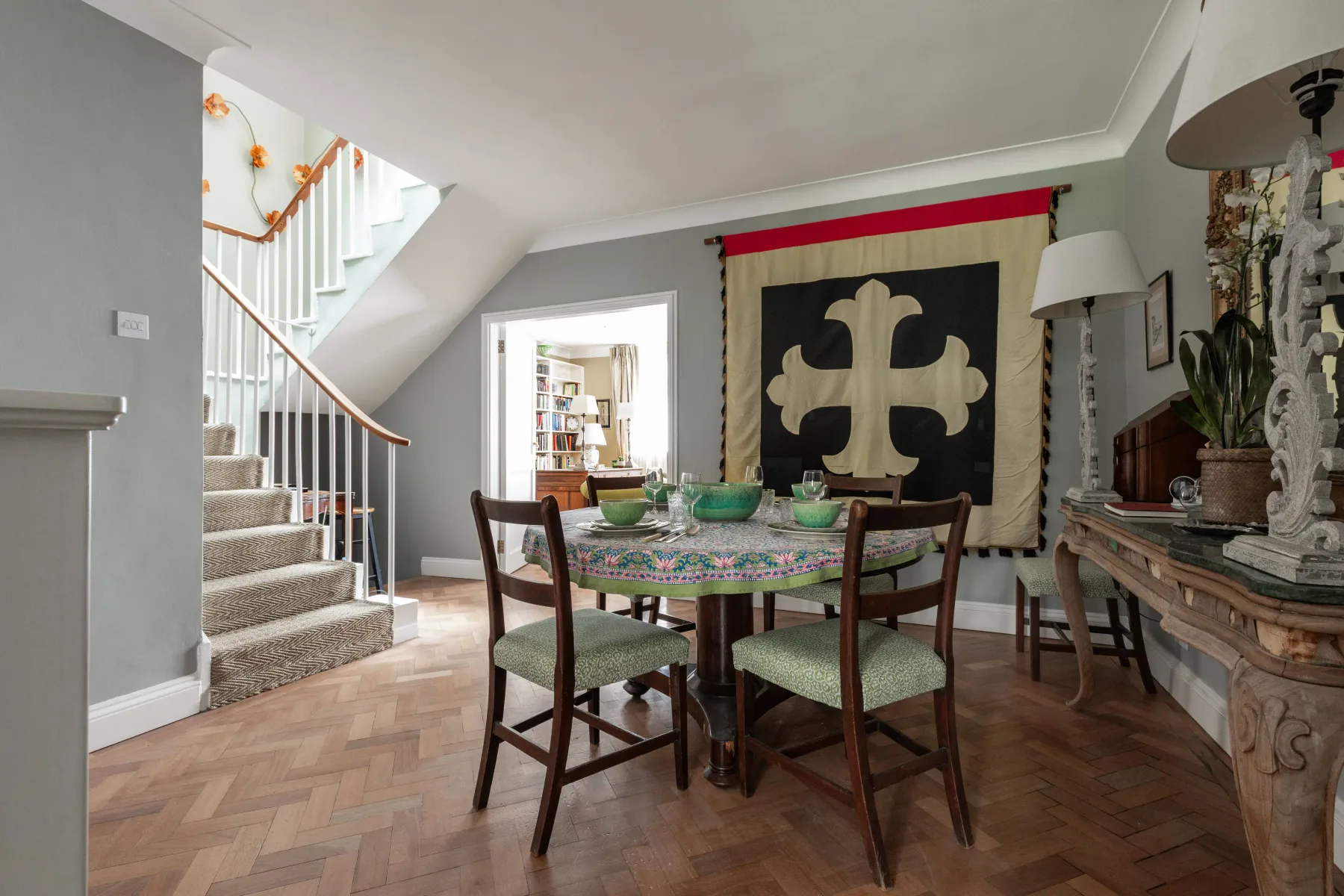 A dining room with a table and chairs beneath a decorative wall hanging.