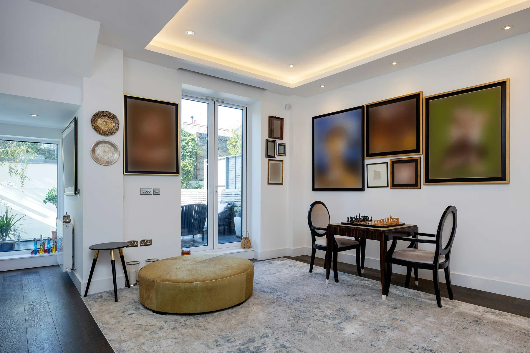 A bright living area with a dining table, framed artwork, and large windows.