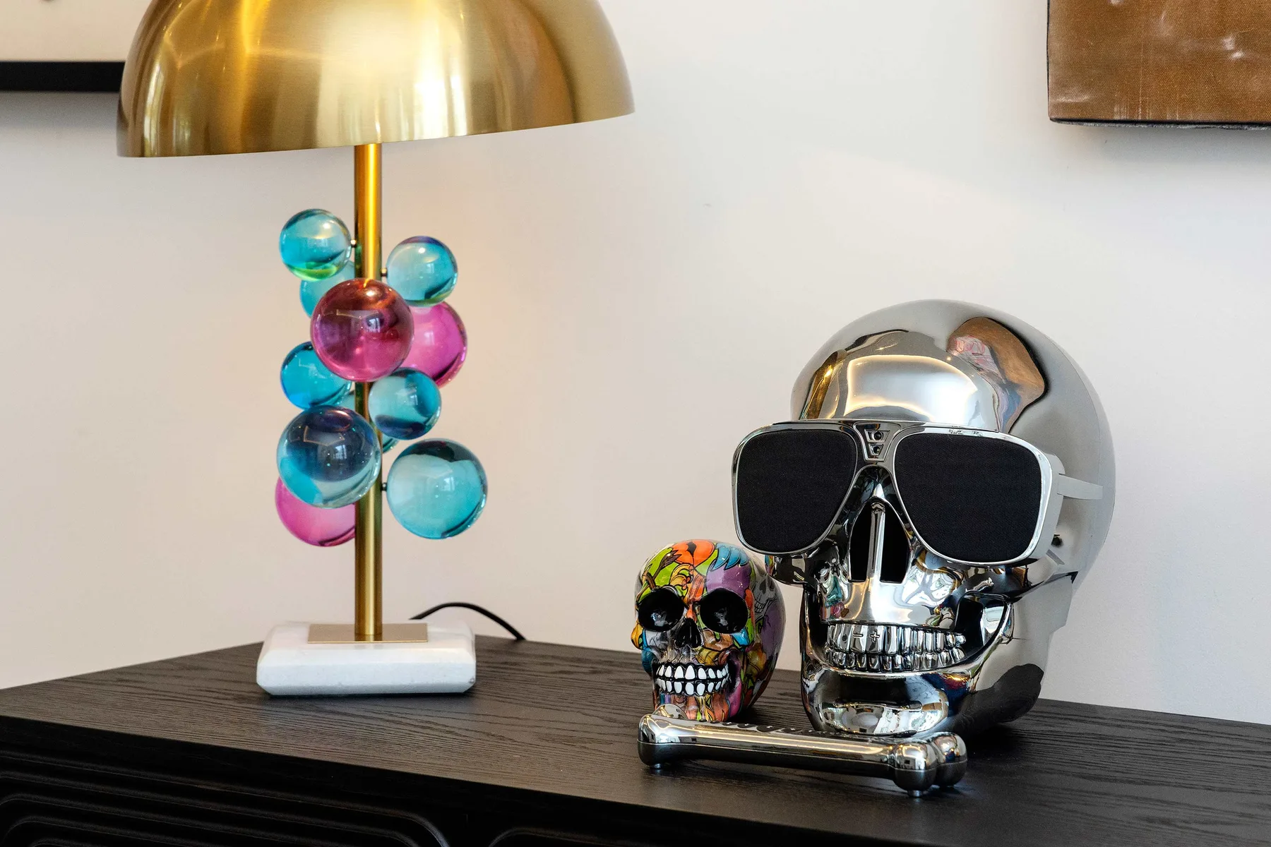 A decorative skull sits on a dark table beside a colorful lamp.