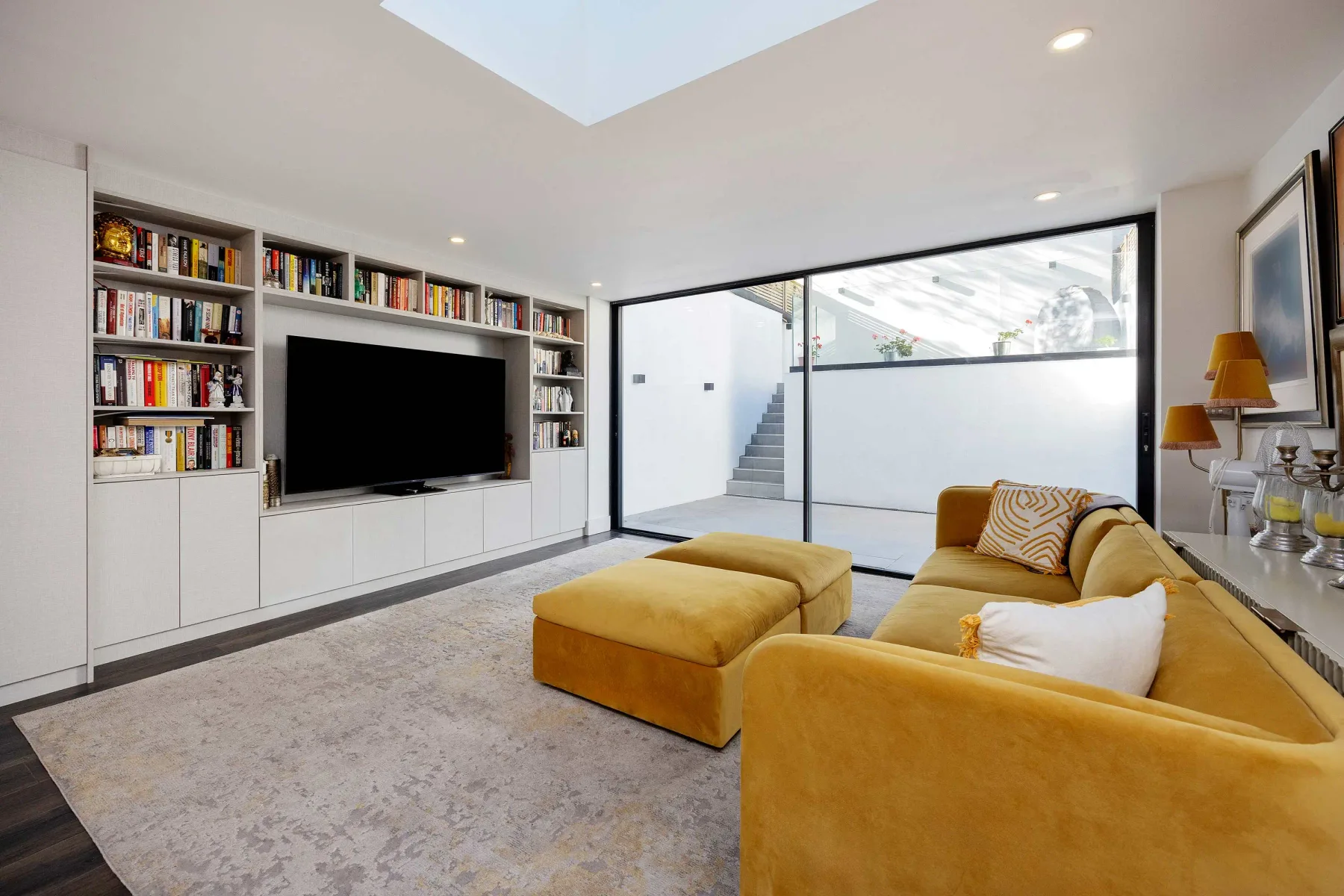 A bright living room with mustard-colored seating and a built-in entertainment wall.