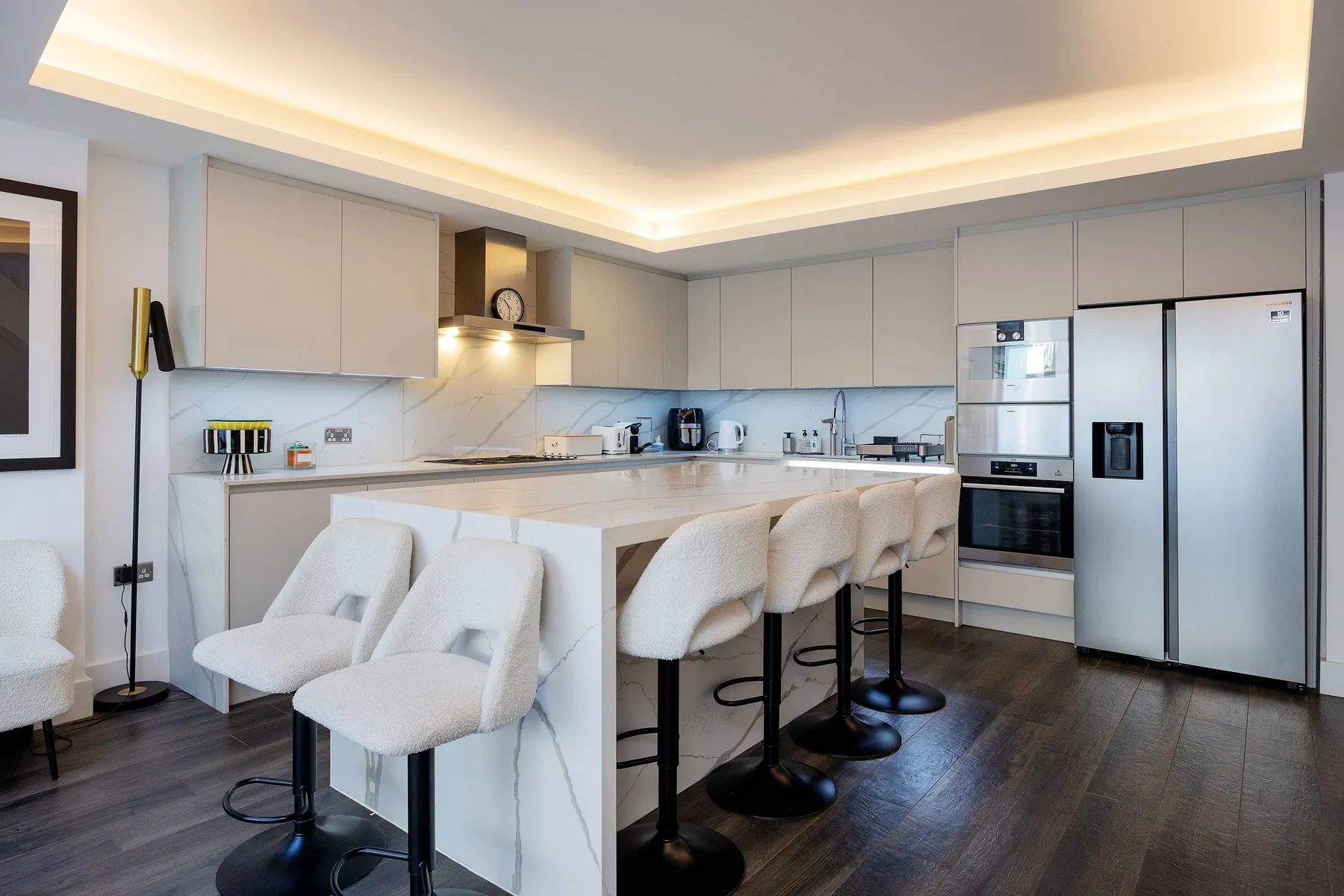 A modern kitchen with a long island and pale upholstered seating.