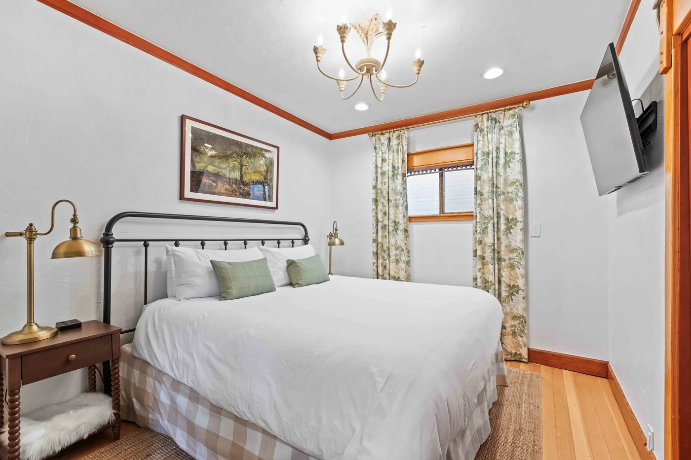 A bedroom with a neatly made bed, patterned curtains, and a wall-mounted television.