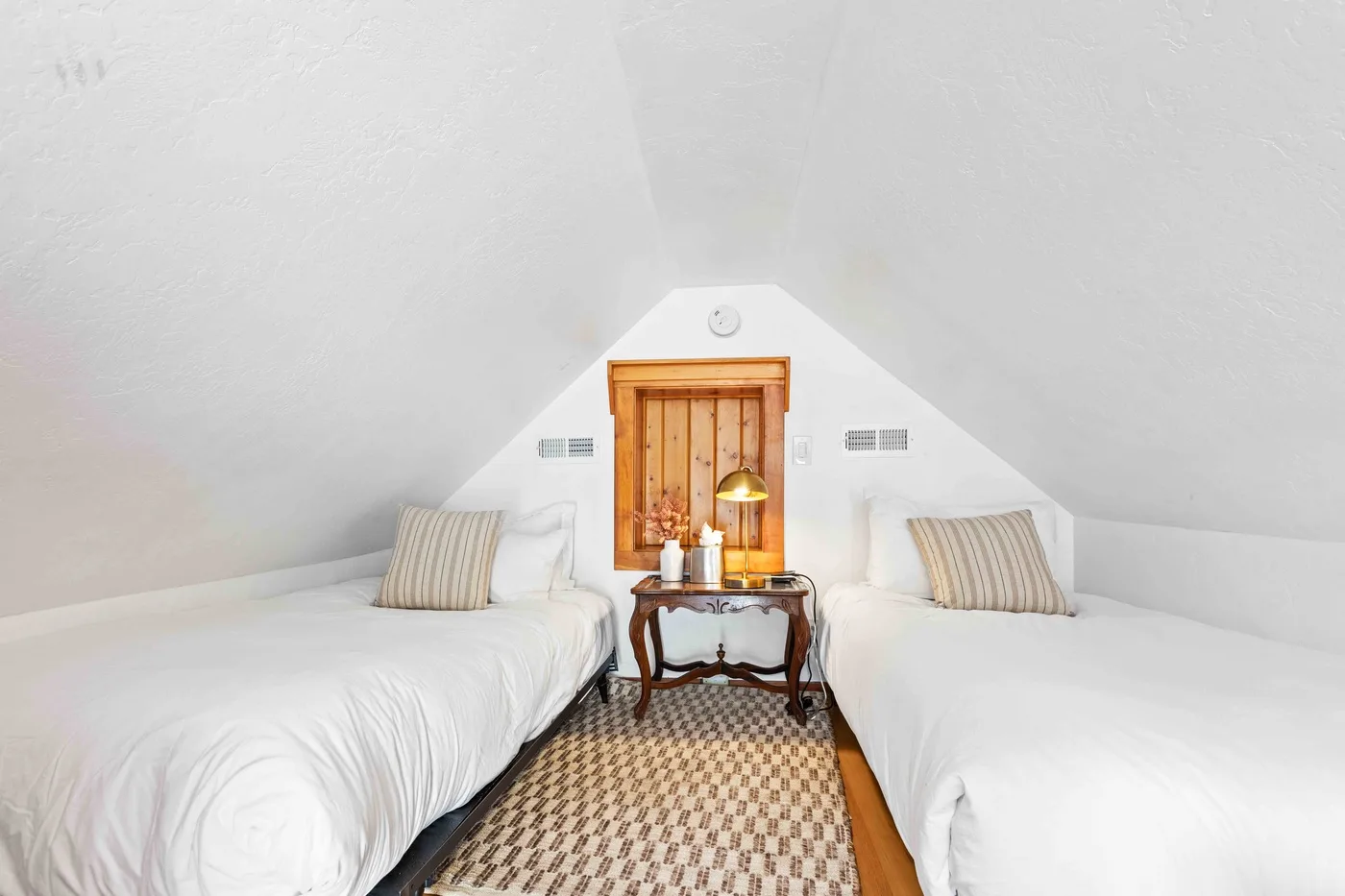 A bright attic bedroom with two beds and a small table between them.