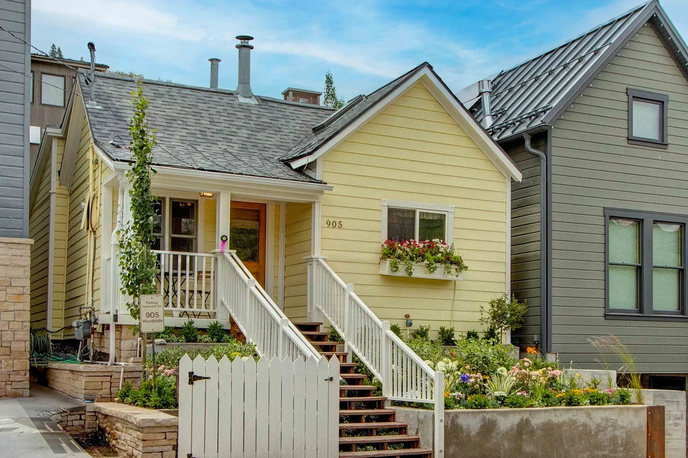 A yellow house with a small front porch, white railings, and garden beds.