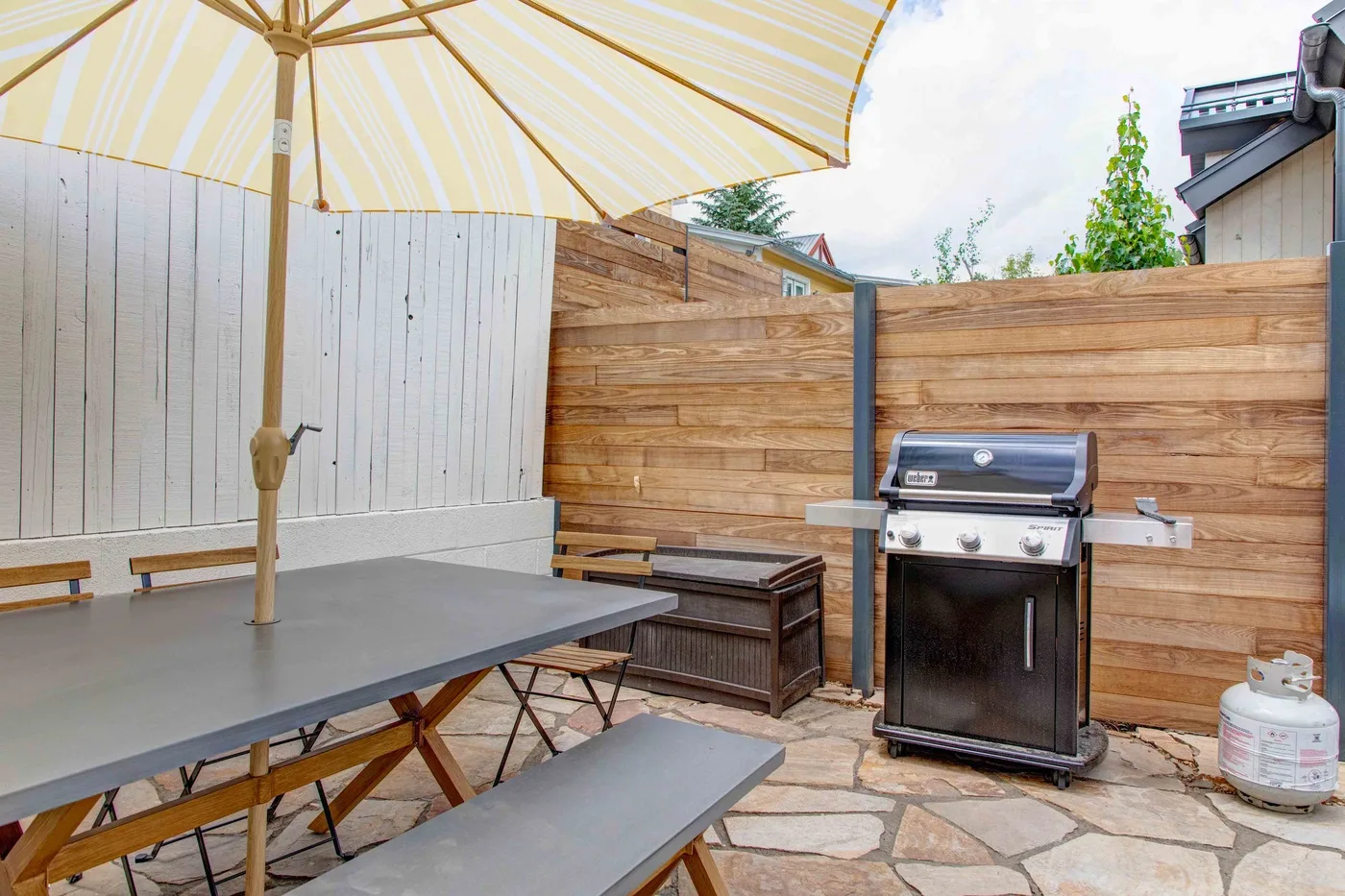 An outdoor patio with a shaded picnic table and a barbecue grill.