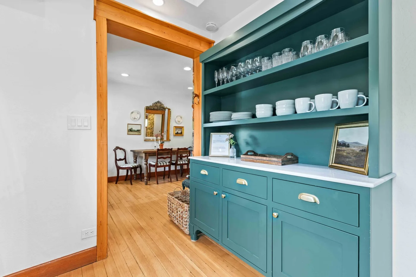 A teal built-in cabinet with open shelves stands beside a dining room.