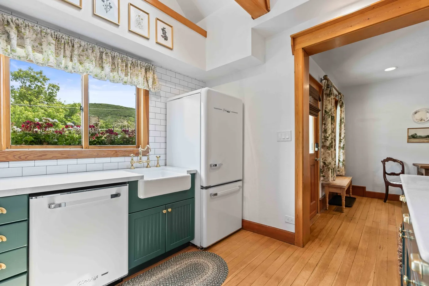 A bright kitchen with green cabinets, a sink, and a window overlooking a garden.