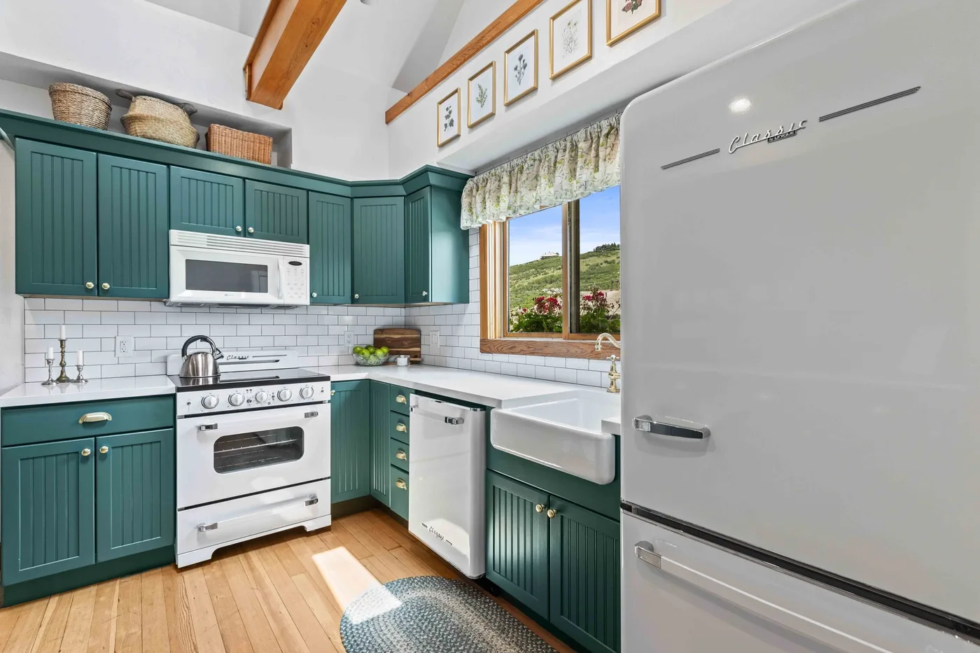 A kitchen with teal cabinets, white appliances, and a window overlooking greenery.
