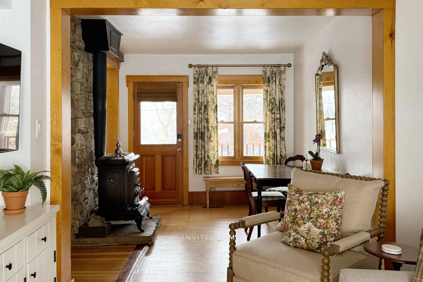 A living room with cushioned seating, a wood stove, and windows.