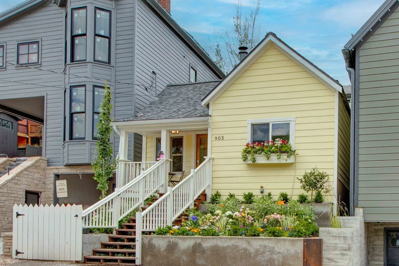 A yellow house with a white porch stands behind a flower garden.