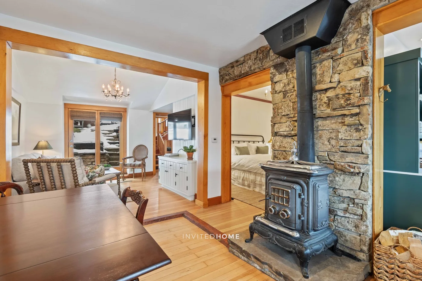 A dining area opens onto a bedroom beside a stone fireplace and wood-burning stove.