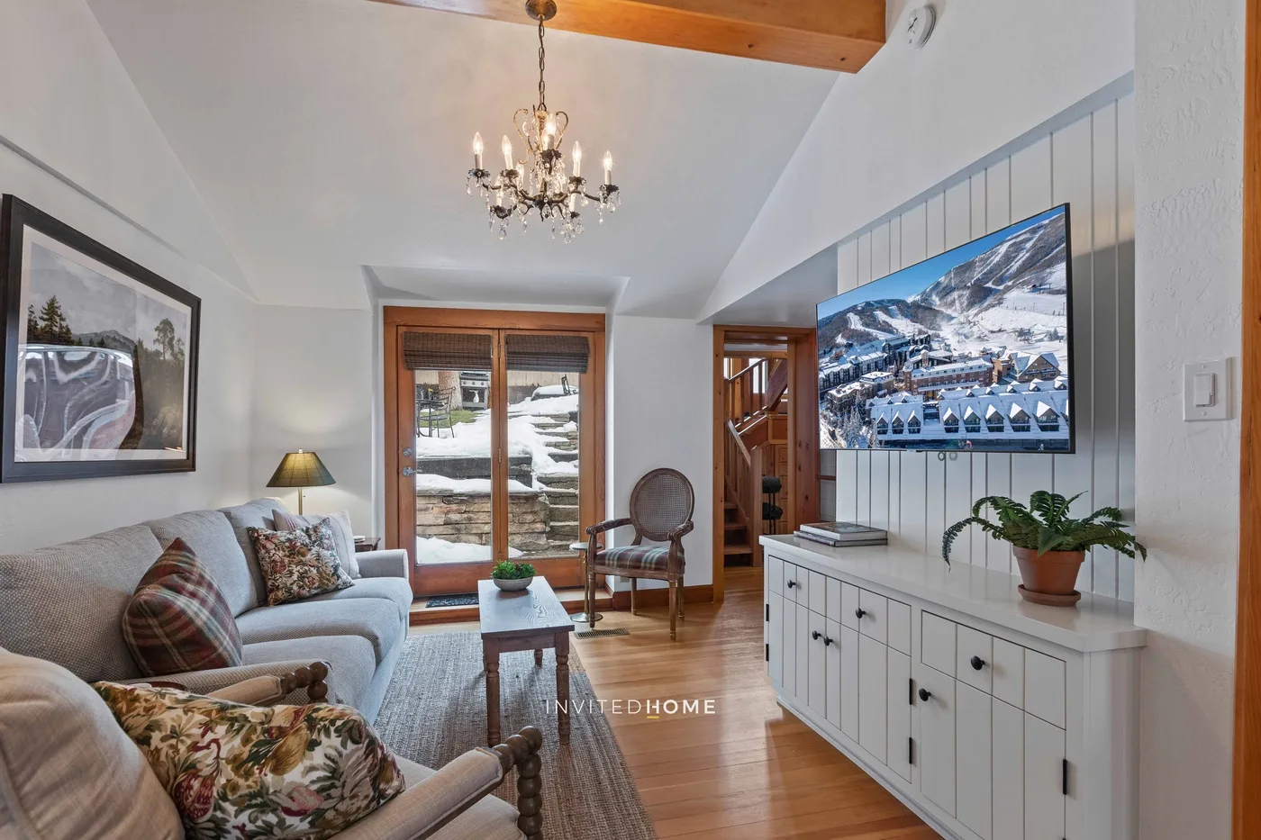 A living room with seating, a television, and glass doors opening onto a snowy view.
