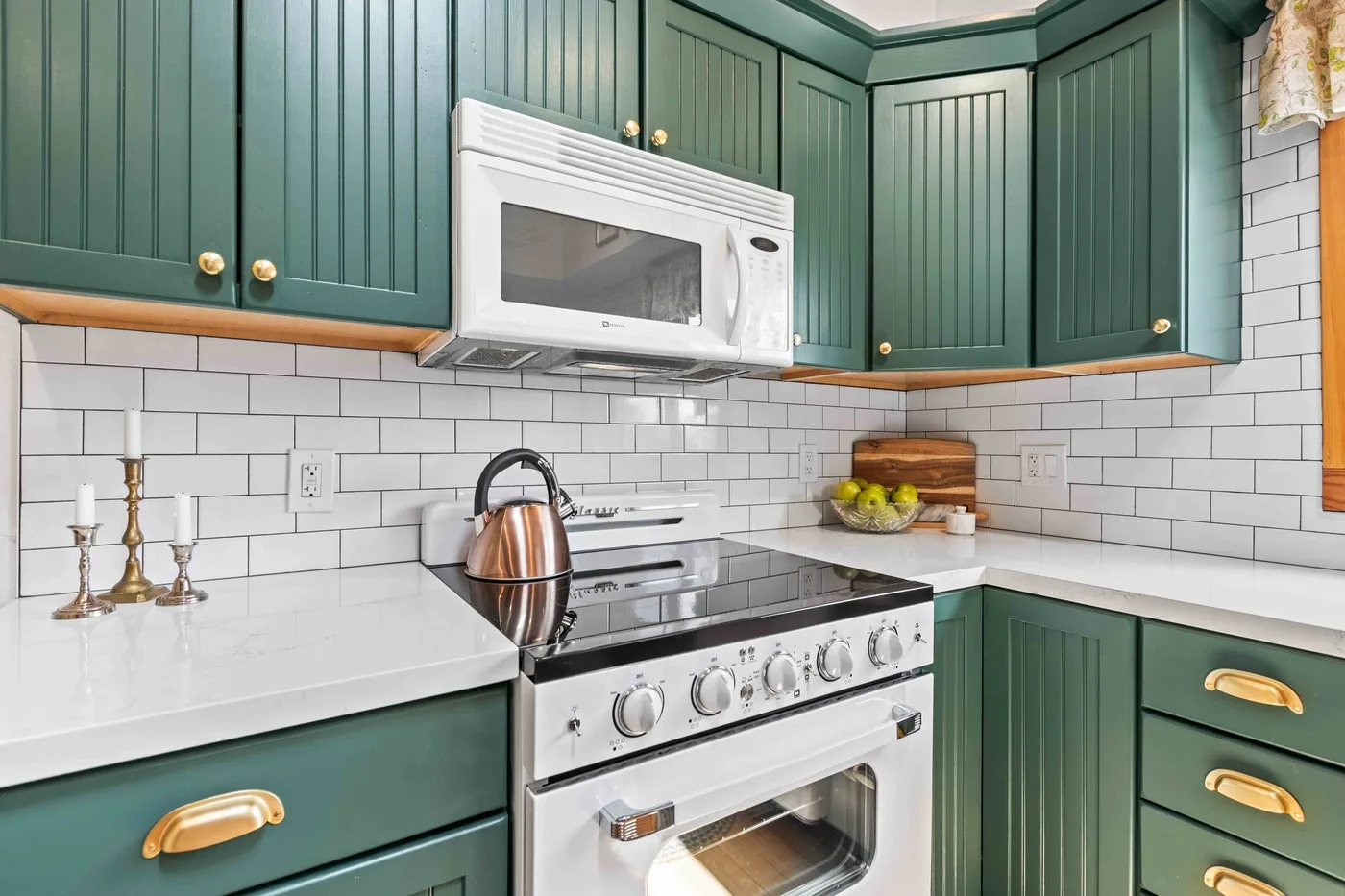A green kitchen with a white range, microwave, and tiled backsplash.