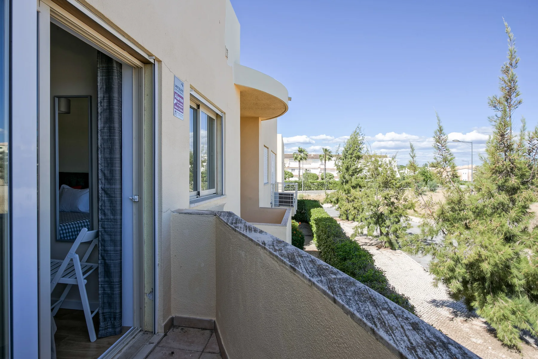 A balcony overlooks landscaped grounds and trees beside the apartment building.