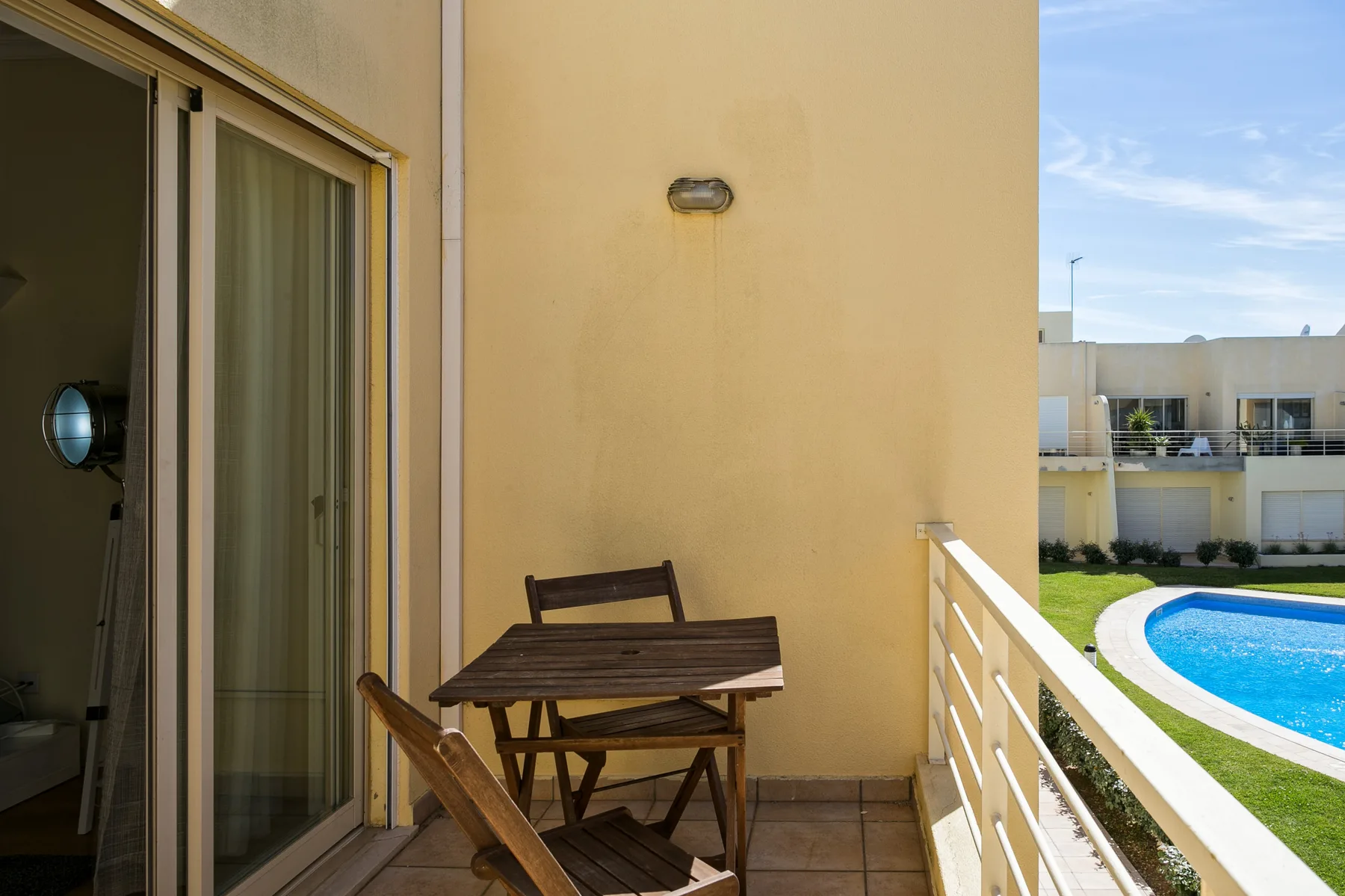 A balcony with a small table and seating overlooks a swimming pool.