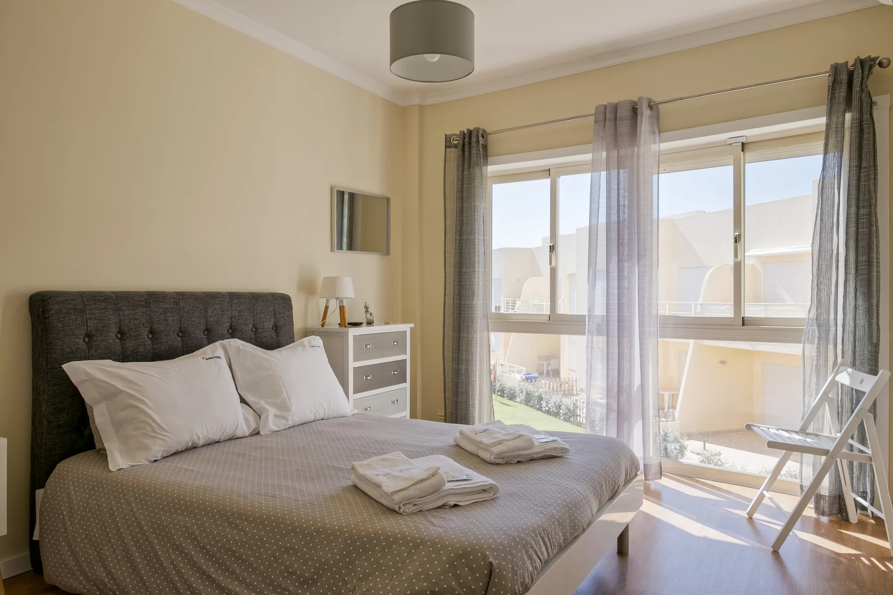 A bright bedroom with a double bed beside glass doors opening onto a balcony.