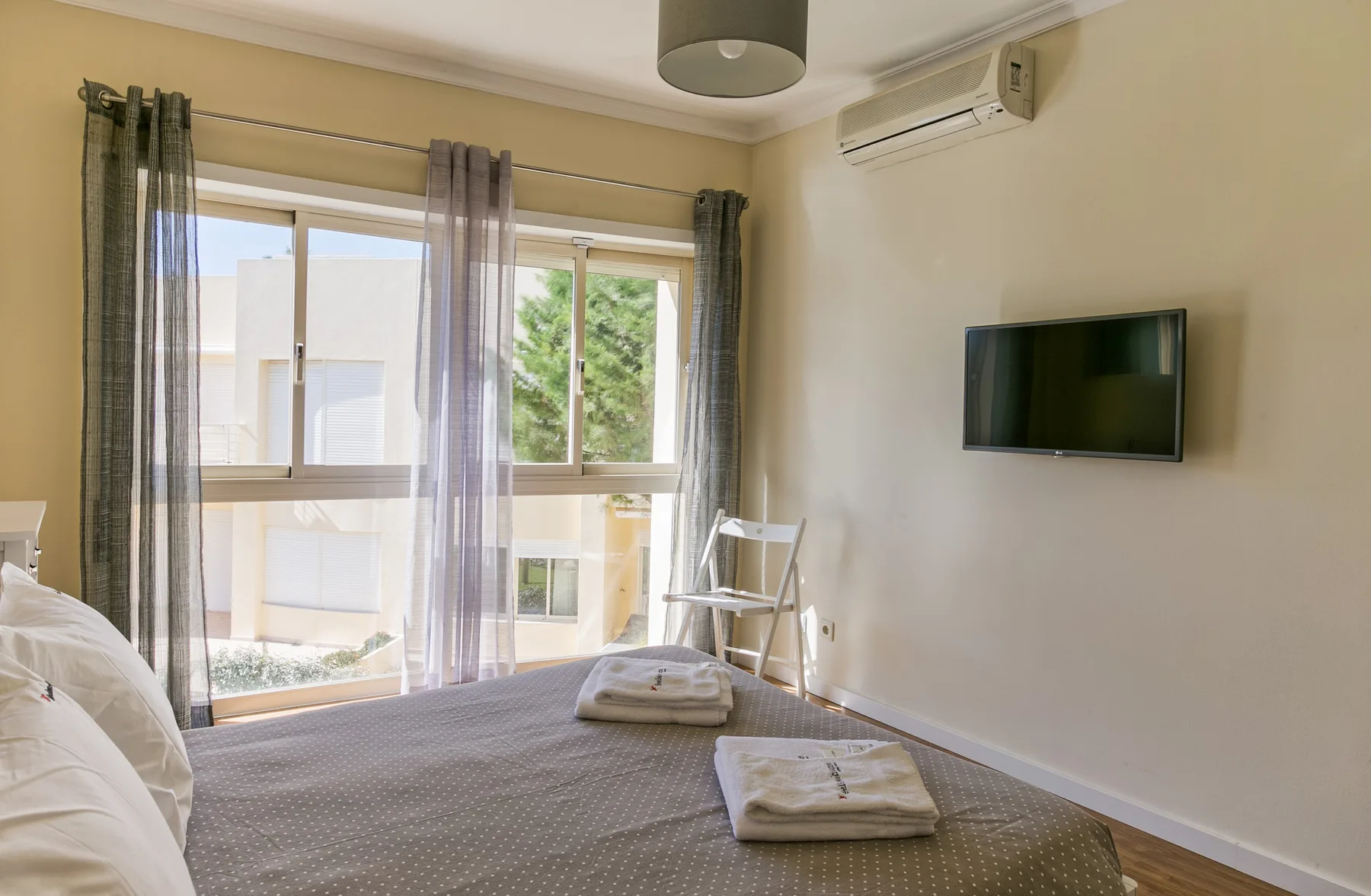 A bedroom with a bed, large windows, and a wall-mounted television.
