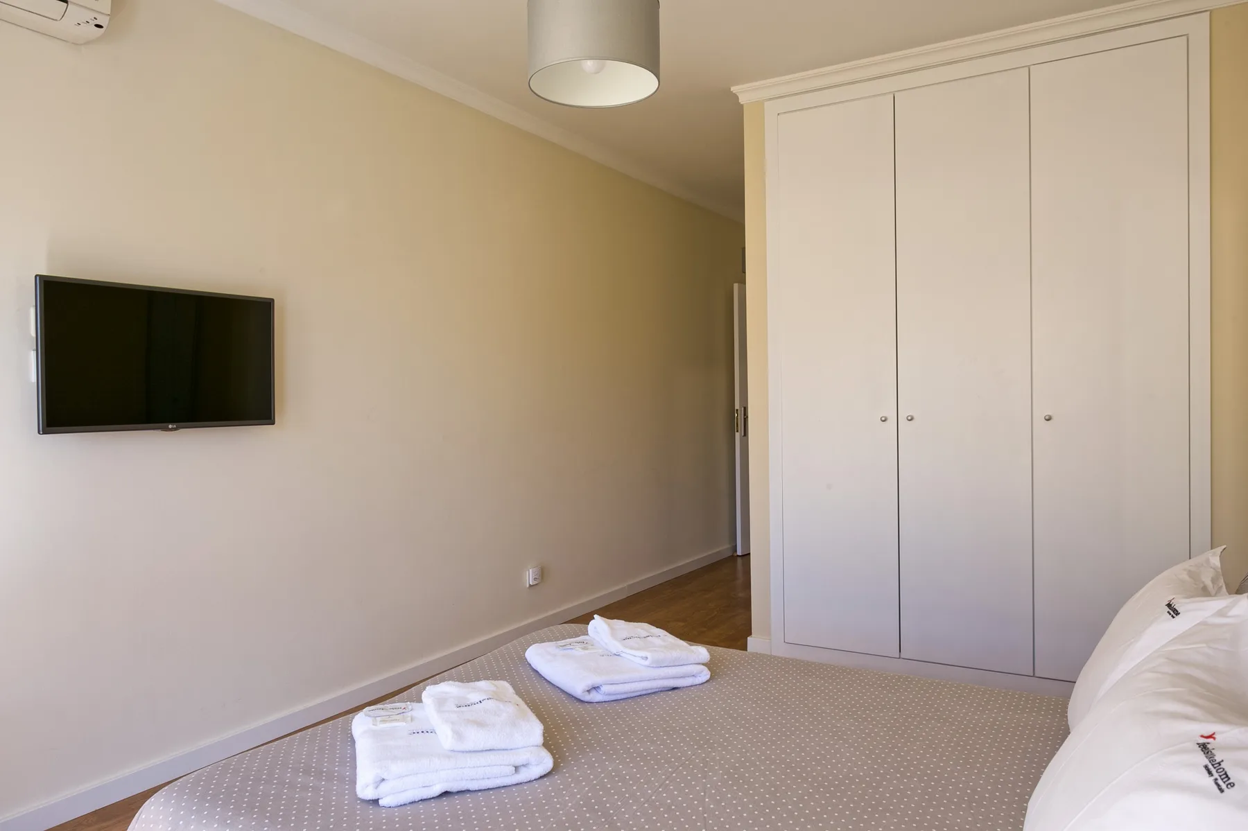 A bedroom with a wall-mounted television, a wardrobe, and folded towels.