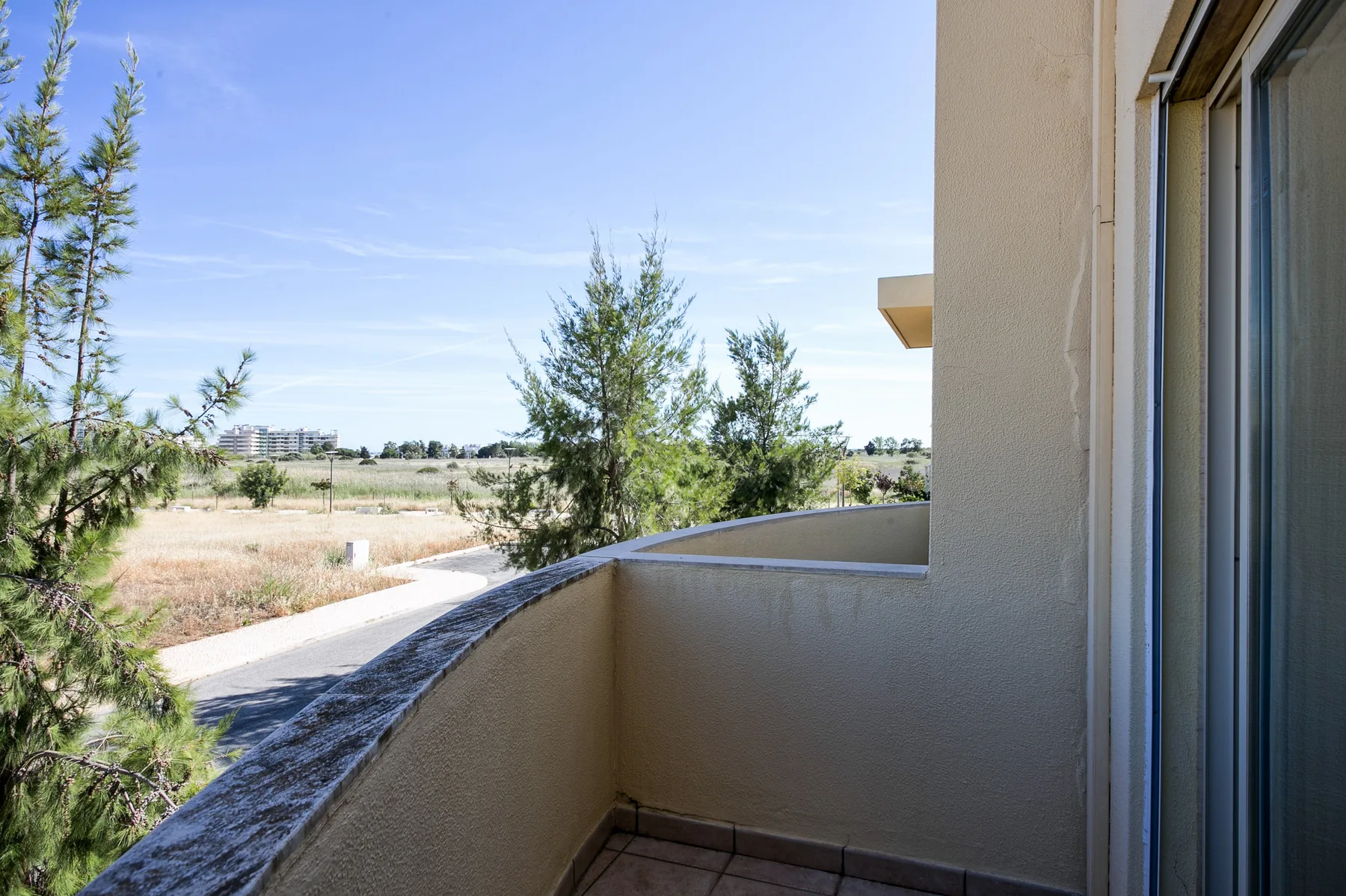 A small balcony overlooks trees and open fields beneath a clear sky.