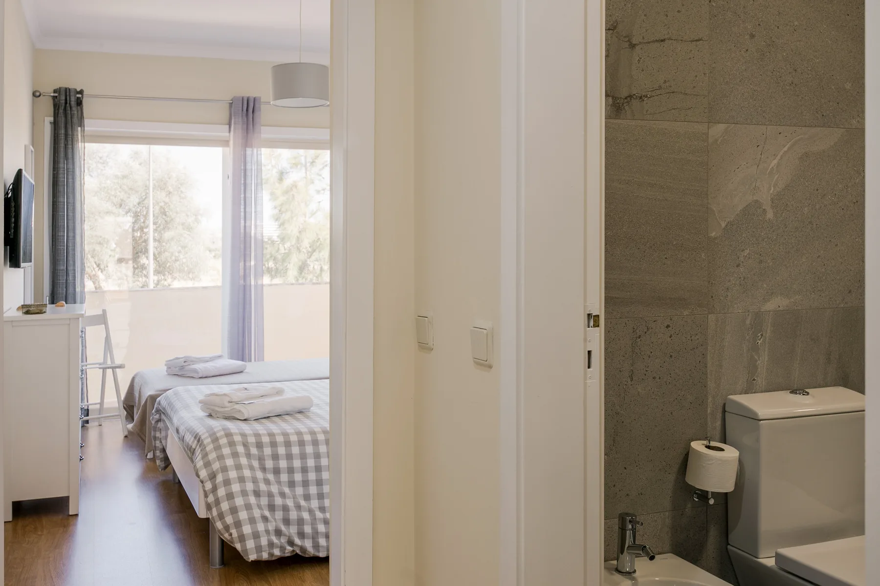 A bedroom with a neatly made bed is visible beside a bathroom.